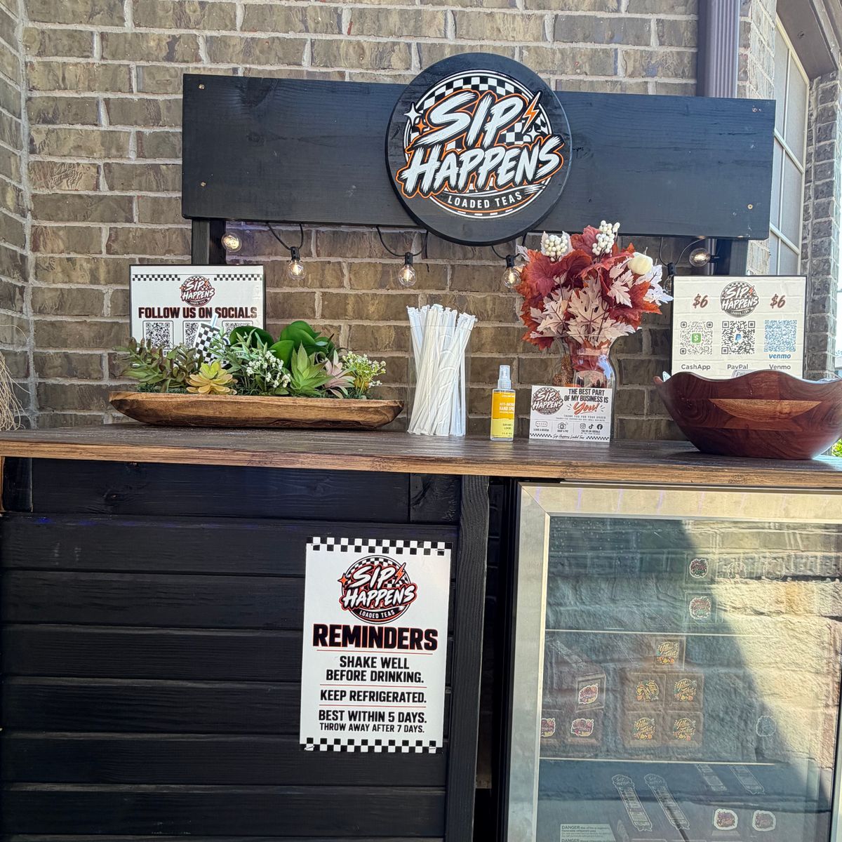 The real Sip Happens front walkway stand with its sign and stocked fridge
